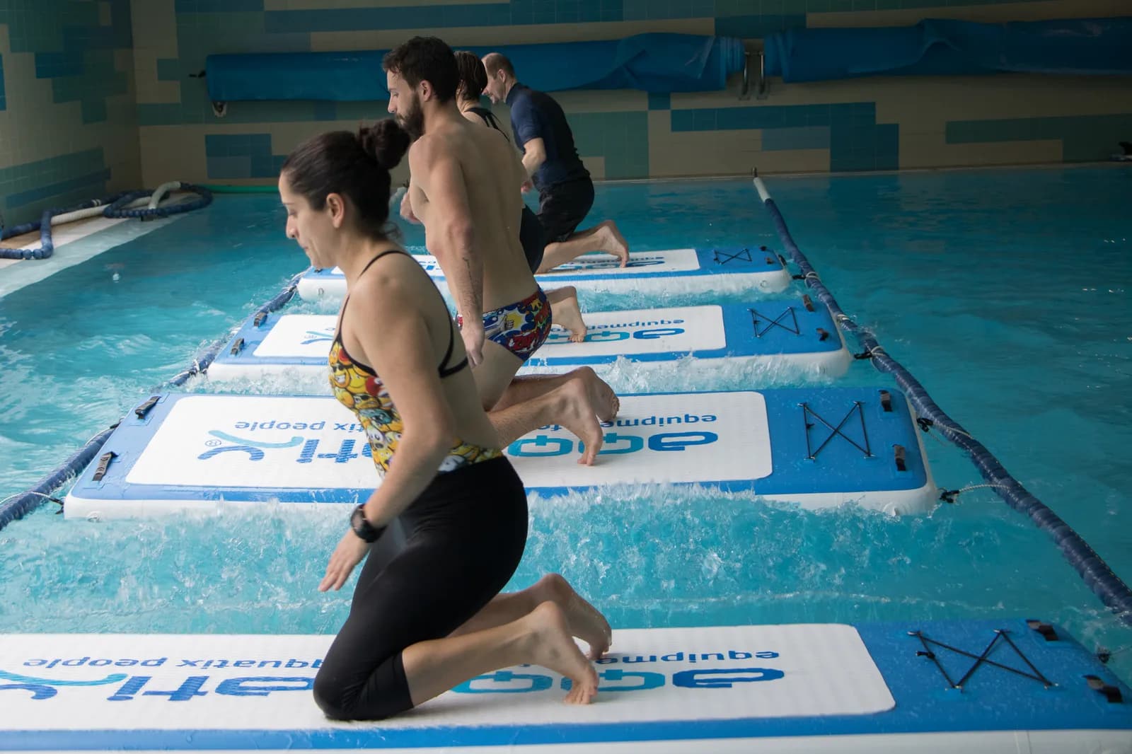 Três participantes a executar um exercício sobre pranchas flutuantes numa piscina
